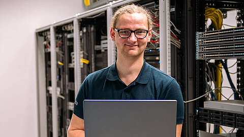 Fachinformatiker Systemintegration (m/w/d) Auszubildender zum Fachinformatiker Systemintegration (m/w/d) steht vor einem Serverschrank und hält ein Laptop in der Hand