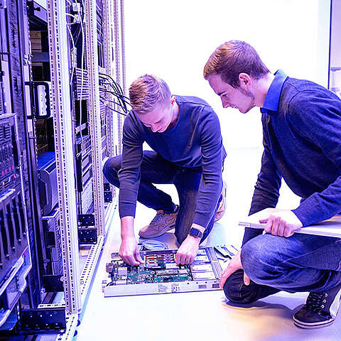 Zwei Mitarbeiter, die vor einem Serverschrank knien und an der Technik arbeiten