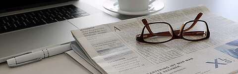 Laptop, Zeitung, Brille und Kaffeetasse auf einem Tisch